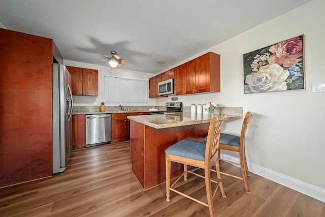 kitchen featuring appliances with stainless steel finishes, hardwood / wood-style flooring, ceiling fan, and a kitchen bar