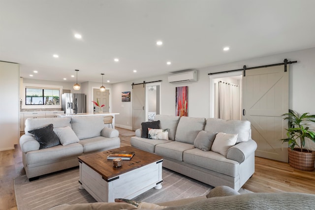 living room with a wall mounted air conditioner, a barn door, and light hardwood / wood-style flooring