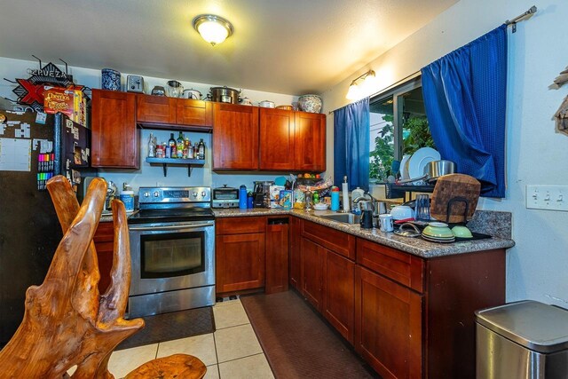 kitchen with sink, black refrigerator, light tile patterned floors, and stainless steel range with electric stovetop