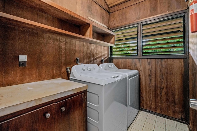 clothes washing area with wooden walls, light tile patterned floors, and washer and dryer