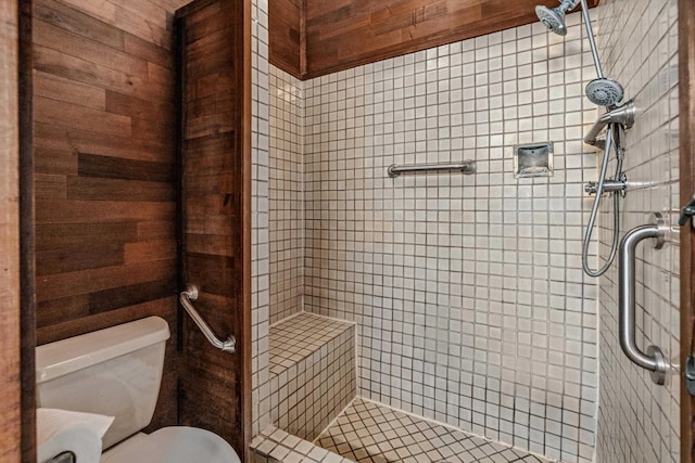 bathroom with wood walls, toilet, and tiled shower