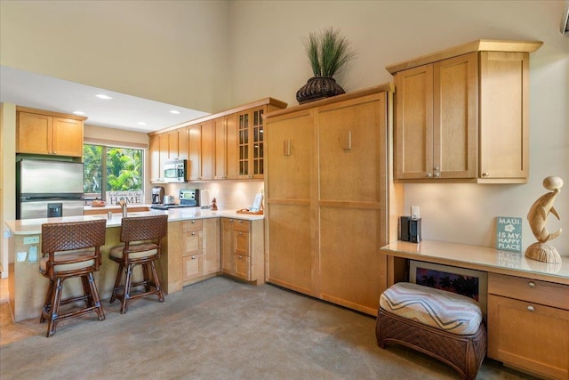 kitchen featuring a breakfast bar area, glass insert cabinets, stainless steel appliances, light countertops, and recessed lighting