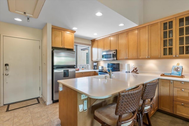 kitchen with glass insert cabinets, a kitchen breakfast bar, stainless steel appliances, light countertops, and recessed lighting