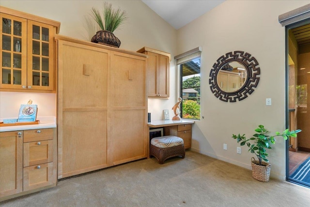 kitchen featuring lofted ceiling, light countertops, light colored carpet, glass insert cabinets, and baseboards