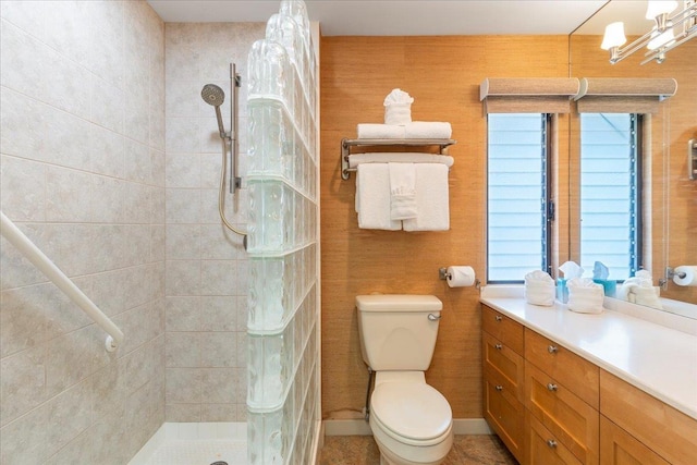 bathroom with baseboards, a tile shower, vanity, and toilet