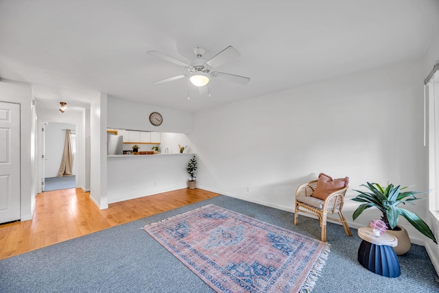sitting room with carpet flooring, baseboards, a ceiling fan, and wood finished floors