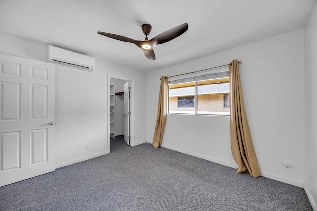 unfurnished bedroom featuring a wall mounted air conditioner, ceiling fan, a spacious closet, carpet floors, and baseboards