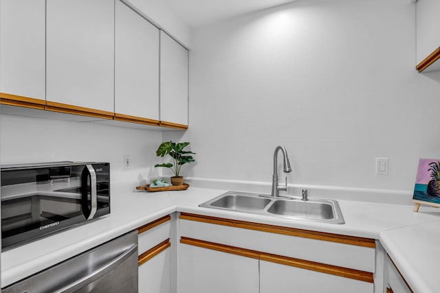 kitchen featuring white cabinets, light countertops, dishwashing machine, and a sink