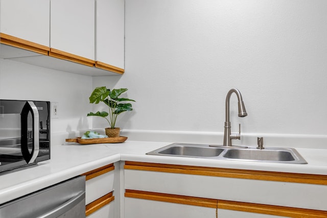 kitchen featuring stainless steel dishwasher, a sink, white cabinetry, black microwave, and light countertops