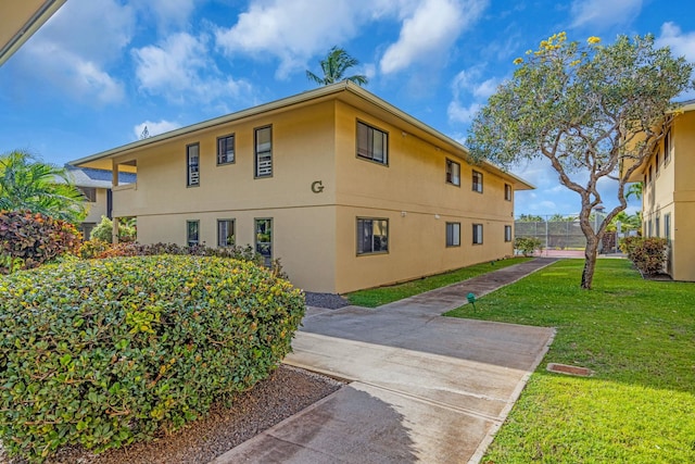 view of side of home with fence, stucco siding, and a lawn