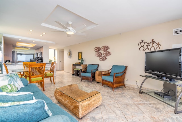 living room with ceiling fan, a tray ceiling, and light tile floors