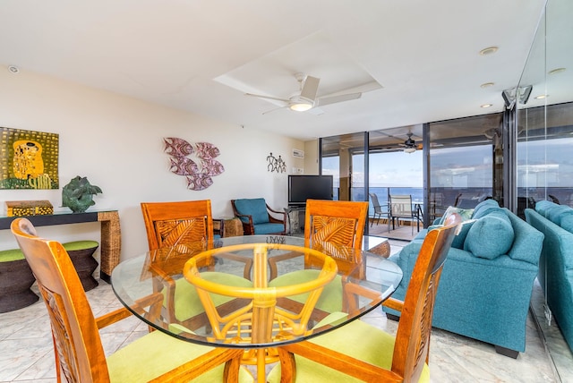 dining area with ceiling fan, light tile flooring, a wall of windows, a water view, and a raised ceiling