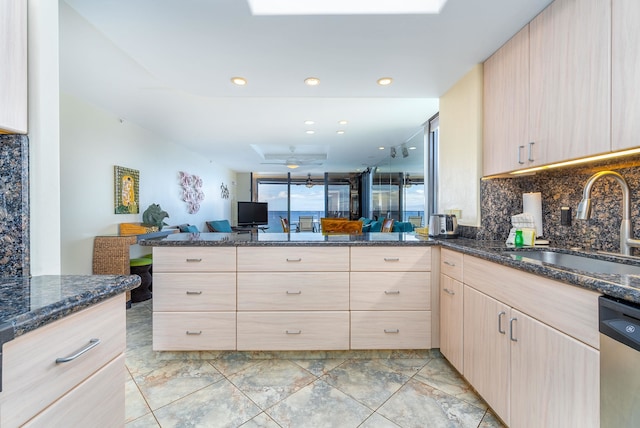 kitchen featuring kitchen peninsula, light brown cabinets, dark stone counters, stainless steel dishwasher, and tasteful backsplash