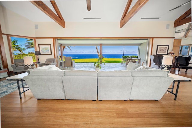 living room with beam ceiling, a towering ceiling, a water view, and light wood-type flooring