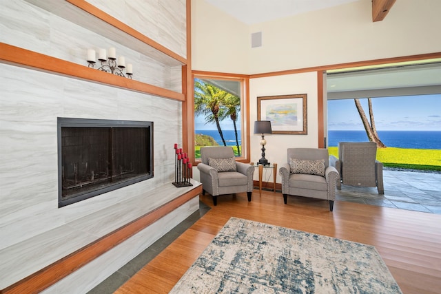 living room featuring a towering ceiling, hardwood / wood-style floors, a tiled fireplace, beamed ceiling, and a water view