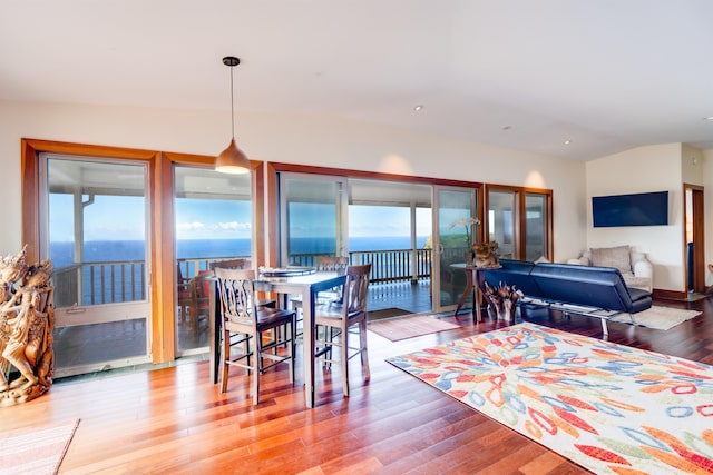 dining space featuring vaulted ceiling, hardwood / wood-style flooring, a water view, and a wealth of natural light