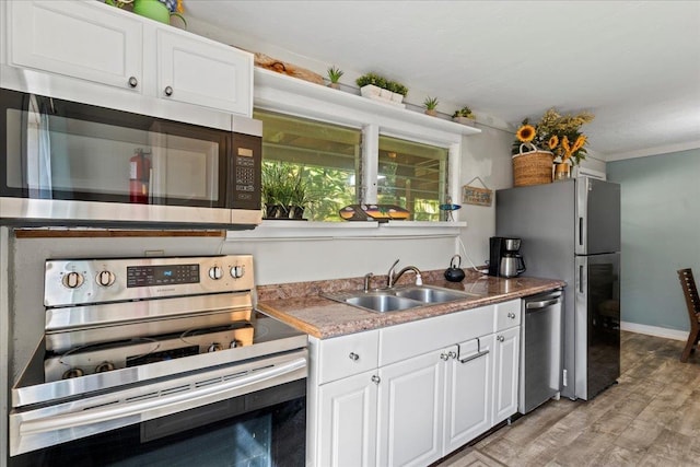 kitchen with appliances with stainless steel finishes, crown molding, sink, light hardwood / wood-style flooring, and white cabinetry