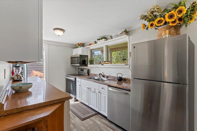 kitchen with sink, dark stone countertops, light hardwood / wood-style floors, white cabinets, and appliances with stainless steel finishes