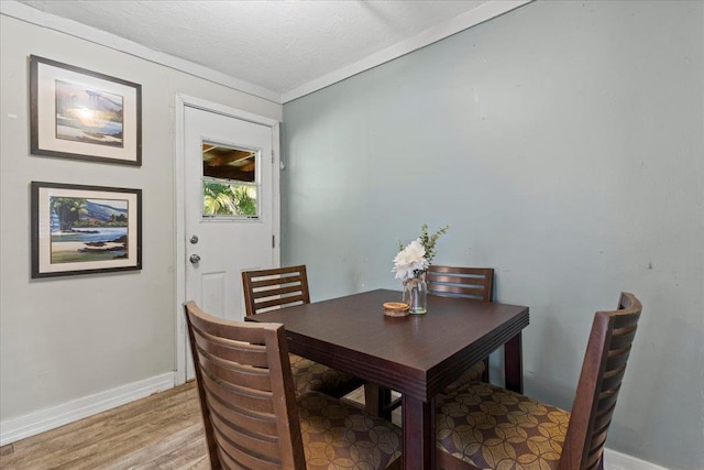 dining space featuring wood-type flooring, a textured ceiling, and ornamental molding