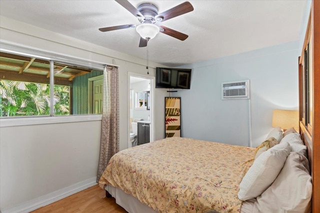 bedroom featuring ceiling fan, wood-type flooring, an AC wall unit, and ensuite bath