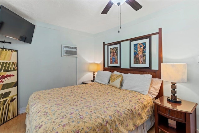 bedroom featuring a wall mounted air conditioner, wood-type flooring, and ceiling fan