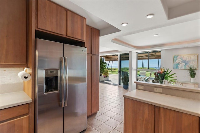 kitchen with a tray ceiling, decorative backsplash, light tile patterned floors, and stainless steel refrigerator with ice dispenser