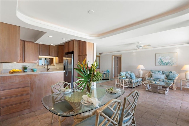 tiled dining room with a raised ceiling, ceiling fan, and sink