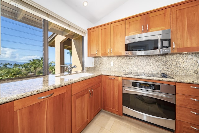 kitchen featuring sink, vaulted ceiling, light stone countertops, appliances with stainless steel finishes, and tasteful backsplash