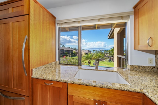 kitchen with paneled built in refrigerator, light stone counters, and sink