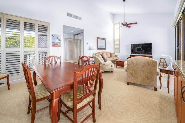 carpeted dining space featuring ceiling fan and a high ceiling