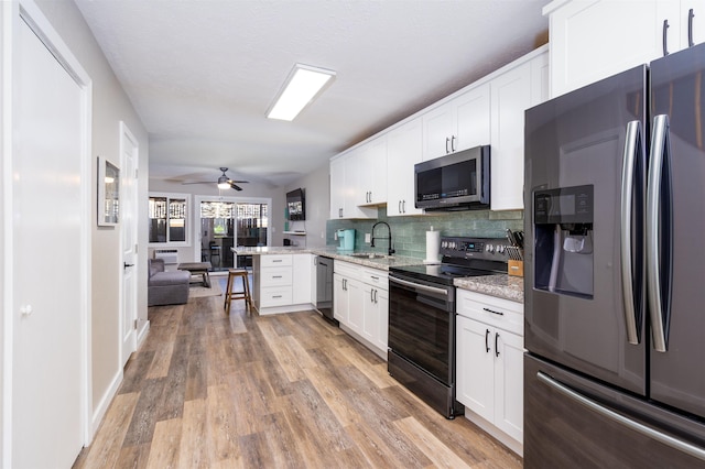 kitchen with sink, white cabinetry, stainless steel appliances, light stone countertops, and kitchen peninsula