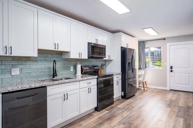 kitchen with white cabinetry, sink, light stone counters, black appliances, and light wood-type flooring