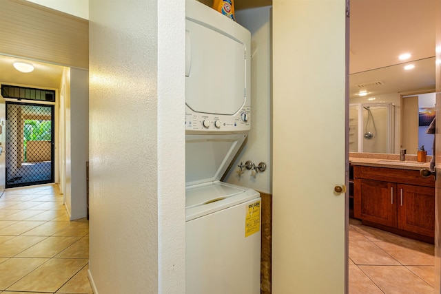 laundry room featuring stacked washer and clothes dryer, light tile patterned floors, a sink, laundry area, and a textured wall