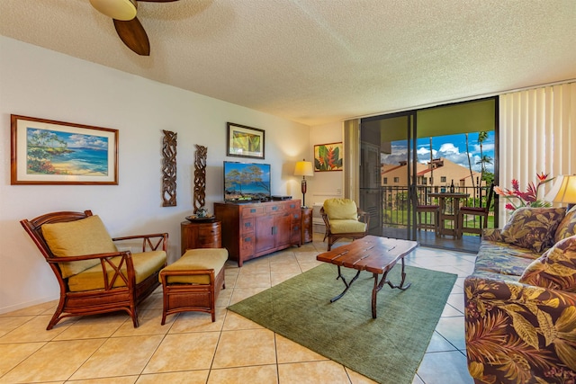 living area featuring a ceiling fan, a wall of windows, light tile patterned floors, and a textured ceiling