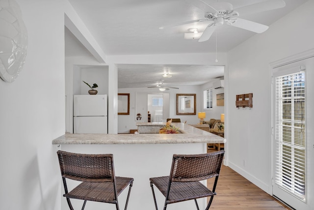 317 Kenolio Rd, Kihei, HI 96753 - kitchen with a ceiling fan, freestanding refrigerator, a breakfast bar area, a peninsula, and a wall mounted air conditioner