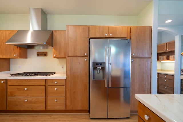 kitchen with stainless steel appliances, wall chimney range hood, and light hardwood / wood-style flooring