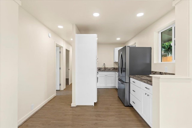 kitchen featuring white cabinets, sink, stainless steel fridge, dark stone countertops, and wood-type flooring