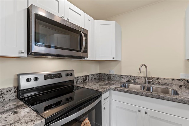 kitchen featuring stainless steel appliances, white cabinetry, dark stone countertops, and sink