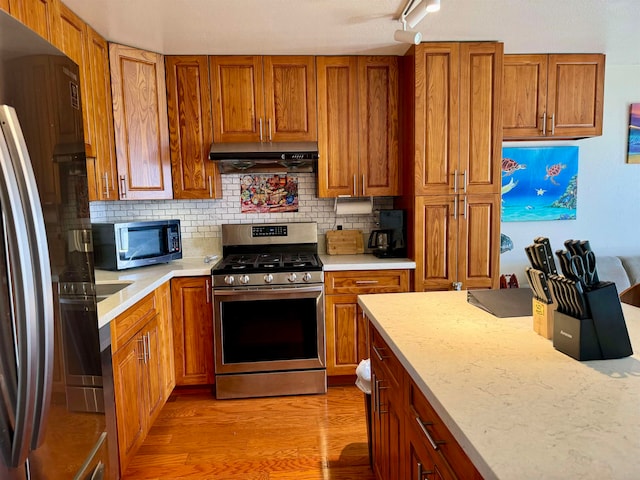 kitchen featuring backsplash, rail lighting, appliances with stainless steel finishes, light stone countertops, and light hardwood / wood-style floors