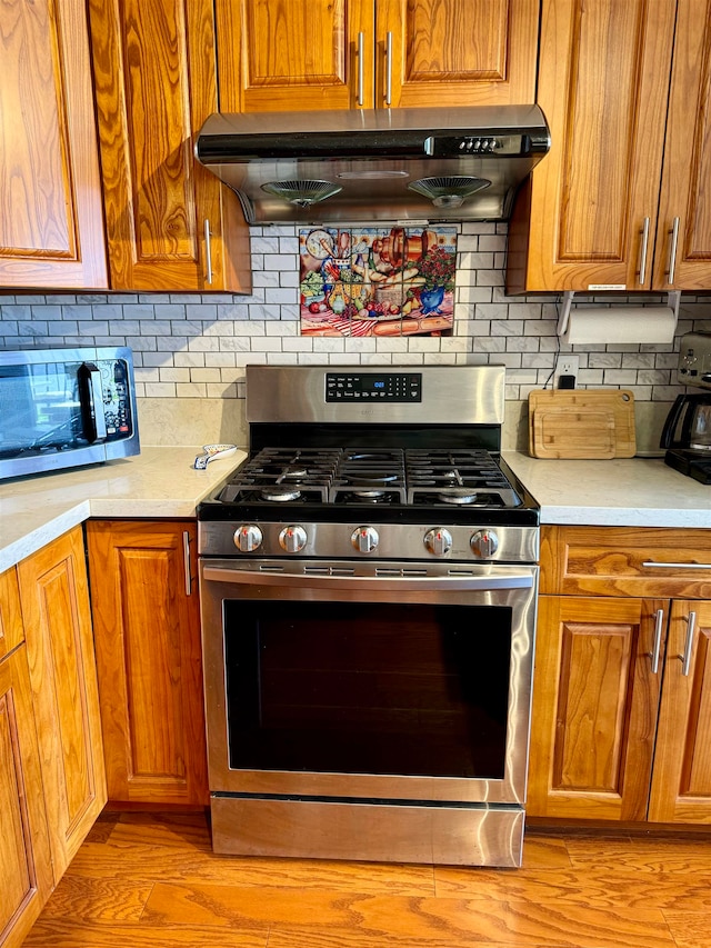 kitchen with appliances with stainless steel finishes, decorative backsplash, and light hardwood / wood-style floors