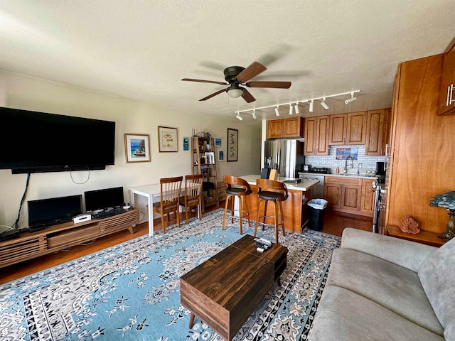 living room with ceiling fan, sink, a textured ceiling, rail lighting, and hardwood / wood-style floors