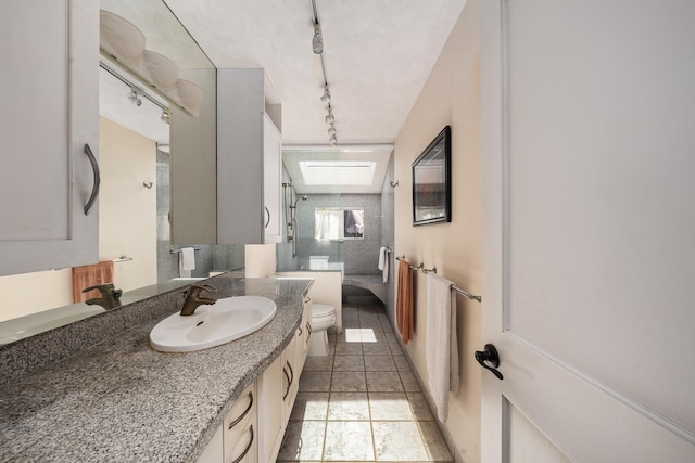 bathroom featuring a skylight, rail lighting, walk in shower, toilet, and vanity