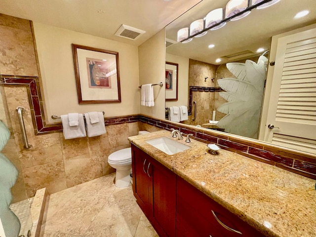 bathroom with tile flooring, vanity with extensive cabinet space, toilet, and tile walls