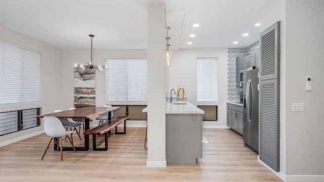 kitchen with pendant lighting, stainless steel fridge with ice dispenser, gray cabinets, light hardwood / wood-style floors, and an inviting chandelier