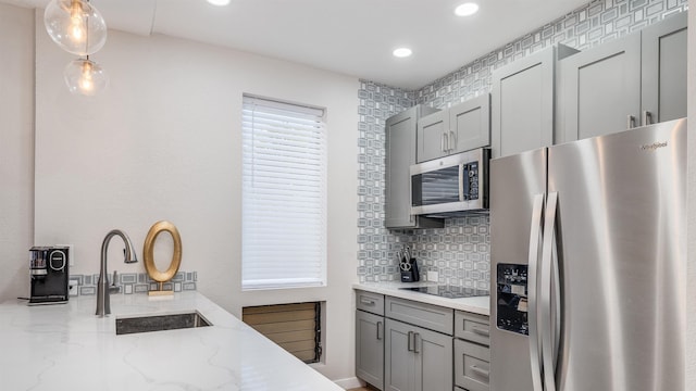 kitchen with appliances with stainless steel finishes, sink, decorative light fixtures, backsplash, and light stone counters