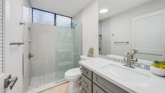 bathroom with tile patterned flooring, toilet, tiled shower, and vanity