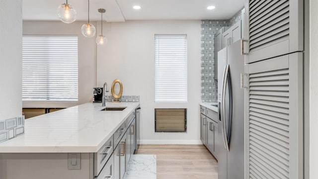 kitchen featuring pendant lighting, appliances with stainless steel finishes, sink, gray cabinetry, and light stone counters