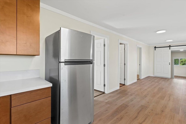 kitchen with stainless steel fridge, ornamental molding, a barn door, and light wood-type flooring