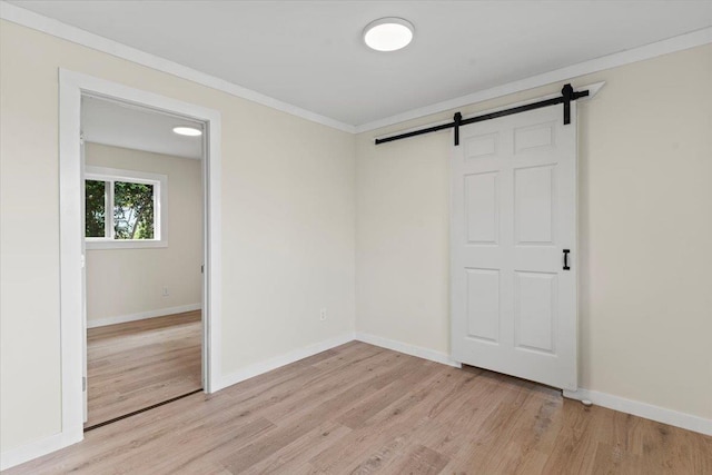 unfurnished room featuring light wood-type flooring, a barn door, and ornamental molding