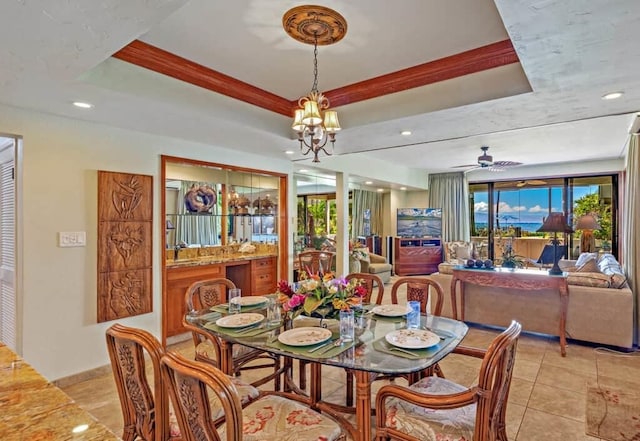 dining area with ceiling fan with notable chandelier, light tile patterned floors, and a tray ceiling